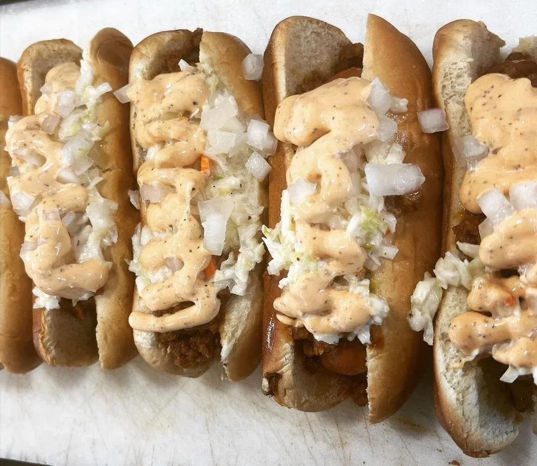 A row of vegan hot dogs topped with chili, slaw and sauce