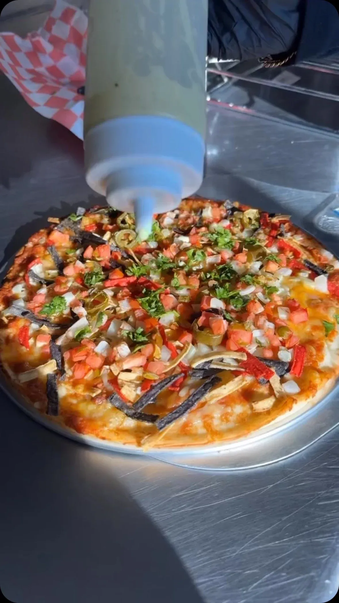 Loaded vegan pizza getting a drizzle of sauce